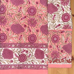 May include: A fabric textile featuring a repeating floral pattern in shades of pink, magenta, and white. The design includes large stylised flower heads, smaller buds, and leafy vines. A horizontal border with a smaller floral motif runs across.