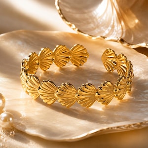 Peut inclure: Un bracelet manchette doré composé d'un motif répétitif de coquilles Saint-Jacques interconnectées. Le métal présente une finition polie et réfléchissante, et le design est ouvert, permettant un ajustement. Le bracelet est de forme circulaire.