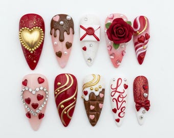 May include: Ten artificial nails with diverse designs, themed for Valentine's Day. Designs include hearts, roses, and the word "Love". The colour palette includes red, pink, white, gold, and brown. Some nails are decorated with glitter, gems, and 3D embellishments.