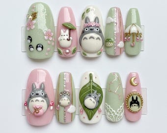 May include: A set of ten artificial nails with a variety of designs. The nails feature a light green, pink, and white color scheme, with 3D character art and floral accents. The designs include Totoro characters, flowers, and other decorative elements.