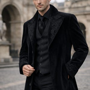 May include: A black velvet coat with ornate embroidery on the lapels and cuffs. The coat is worn over a black vest, shirt, and tie. The outfit is completed with black trousers. The overall style is formal and elegant.