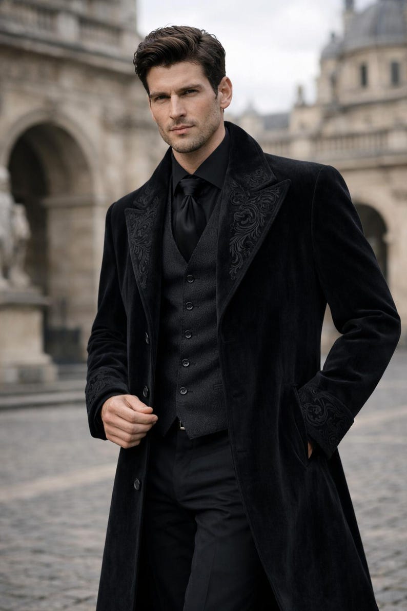 May include: A black velvet coat with ornate embroidery on the lapels and cuffs. The coat is worn over a black vest, shirt, and tie. The outfit is completed with black trousers. The overall style is formal and elegant.