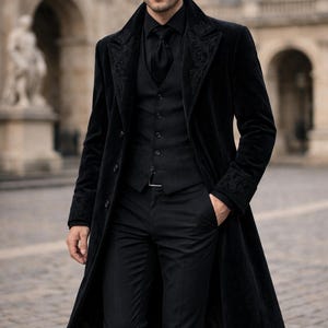 May include: A black velvet coat with ornate embroidery on the lapels and cuffs, worn over a matching black vest, shirt, tie, and trousers. The ensemble is completed with a black belt. The outfit is suitable for formal occasions.