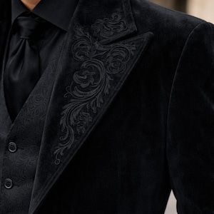 May include: Black velvet suit with ornate embroidered detailing on the lapel and vest. The suit includes a black tie and a black collared shirt. The suit is a formal style.