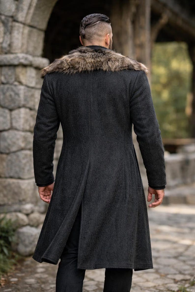 May include: A dark gray wool coat with a faux fur collar. The long coat has a tailored fit and a split back. The person is facing away from the camera, and the background is a stone wall and greenery.