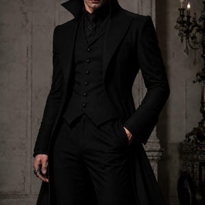May include: A black suit ensemble featuring a long coat, vest, and trousers. The coat has a wide collar and the vest is buttoned. The outfit is completed with a black shirt and a ring. The overall style is gothic and elegant.