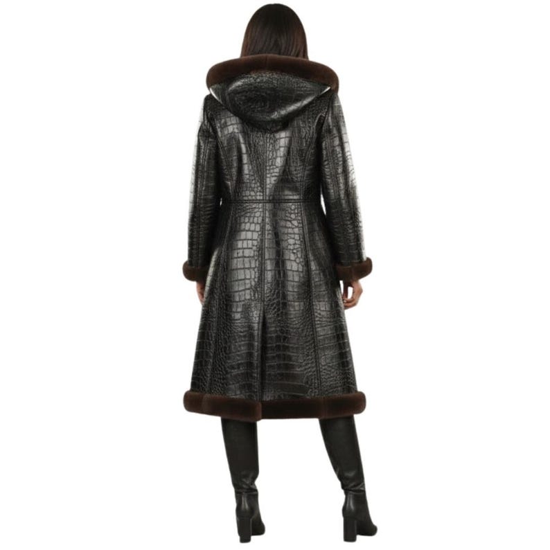 May include: A long, black, crocodile-textured coat with a hood and brown fur trim. The coat is knee-length and has a flared skirt. The model is wearing black boots. The coat is made of a leather-like material.