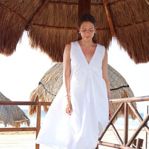 Peut inclure: Une robe midi blanche sans manches dot&eacute;e d'un d&eacute;collet&eacute; en V profond avec une bordure en dentelle d&eacute;licate et un panneau central triangulaire en broderie anglaise sur le corsage. La robe pr&eacute;sente une coupe d&eacute;contract&eacute;e et fluide sous les genoux.