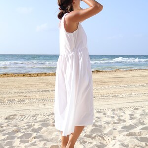Peut inclure: Une robe midi blanche sans manches avec une encolure ronde, un corsage ajust&eacute; et une jupe ample et fluide qui tombe sous les genoux. Le v&ecirc;tement pr&eacute;sente un design simple et &eacute;pur&eacute;, mettant en valeur une couleur blanche unie sur tout le tissu.