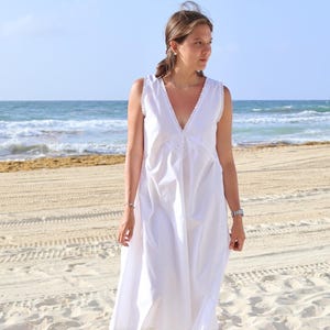 Peut inclure: Une robe midi blanche sans manches avec un d&eacute;collet&eacute; en V profond orn&eacute; d'une fine bordure en dentelle et un d&eacute;tail floral brod&eacute; au centre du corsage. La robe pr&eacute;sente une silhouette d&eacute;contract&eacute;e et fluide qui tombe sous le genou.