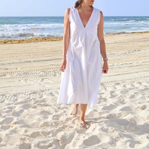 Peut inclure: Une robe midi blanche sans manches dot&eacute;e d'un d&eacute;collet&eacute; en V profond avec une fine bordure en dentelle. La robe pr&eacute;sente une silhouette d&eacute;contract&eacute;e et fluide avec des d&eacute;tails fronc&eacute;s subtils au niveau du corsage et un design &eacute;pur&eacute;.