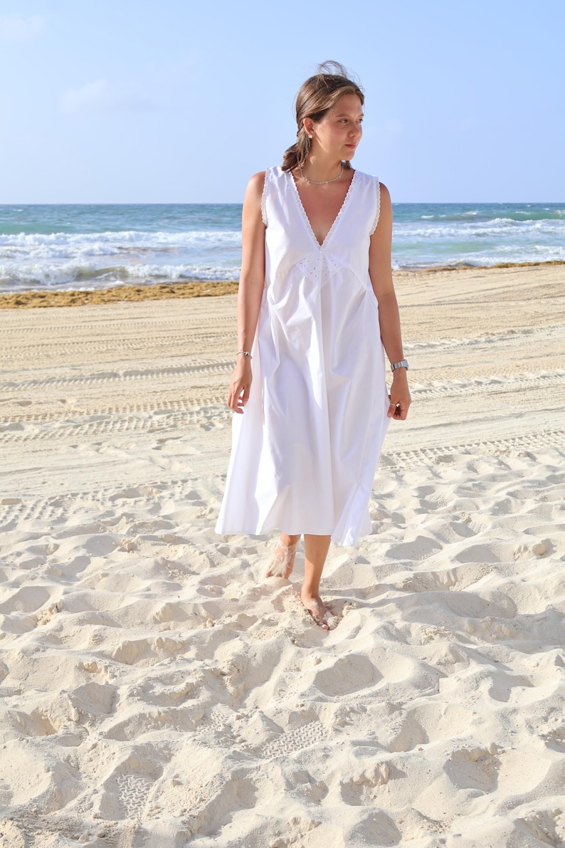 Peut inclure: Une robe midi blanche sans manches dot&eacute;e d'un d&eacute;collet&eacute; en V profond avec une fine bordure en dentelle. La robe pr&eacute;sente une silhouette d&eacute;contract&eacute;e et fluide avec des d&eacute;tails fronc&eacute;s subtils au niveau du corsage et un design &eacute;pur&eacute;.