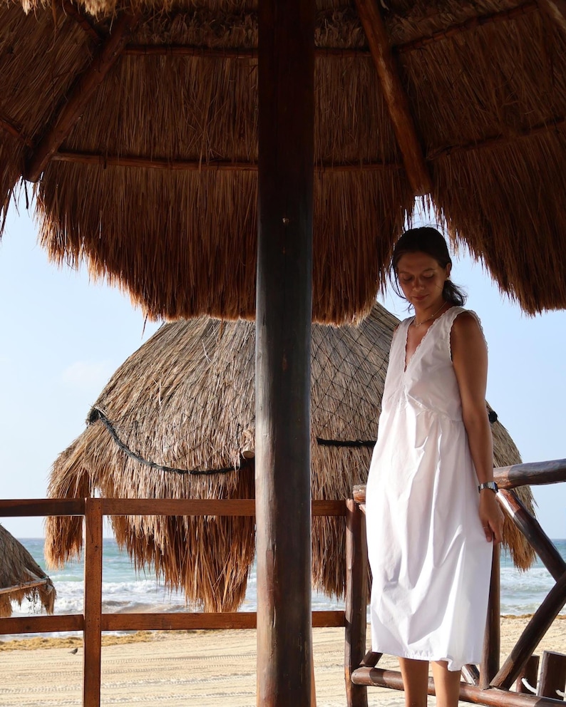 Peut inclure: Une robe midi blanche sans manches avec une encolure en V orn&eacute;e de d&eacute;tails en dentelle d&eacute;licate sur les bords. La robe pr&eacute;sente une silhouette d&eacute;contract&eacute;e et fluide qui tombe sous les genoux, confectionn&eacute;e dans un tissu blanc uni l&eacute;ger.