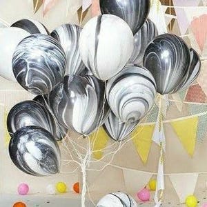 May include: A group of black and white marble balloons. The balloons are tied together and are floating in the air.