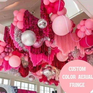 Könnte beinhalten: Eine Deckeninstallation mit rosa und roten Ballons, Discokugeln und Fransen. Die Farbpalette umfasst verschiedene Rosatöne und silberne Akzente. Text auf einem rosa Kreis lautet "CUSTOM COLOR AERIAL FRINGE".