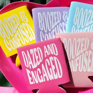 May include: A set of six colorful can coolers with white text. The coolers feature the phrases "Boozed & Confused" and "Dazed and Engaged".