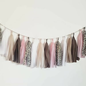 May include: A garland of tissue paper tassels in pink, brown, white, and leopard print. The tassels are strung on a twine string.