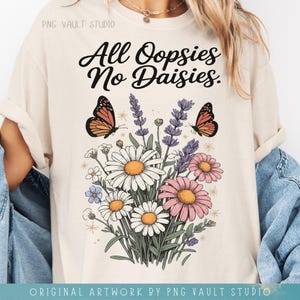 May include: Cream-colored t-shirt featuring a floral design with daisies, pink flowers, and lavender. Two orange and black butterflies are present. The text "All Oopsies No Daisies" is written in black script.