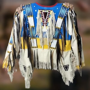 Könnte beinhalten: Ein Kleidungsstück im indianischen Stil mit einem blauen Joch und rotem Besatz. Das Kleidungsstück hat weiße, gelbe und schwarze Akzente mit Fransen und Perlenarbeiten. Die Ärmel und der Saum sind gefranst.