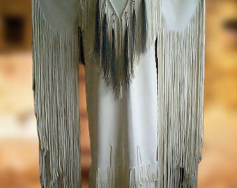 May include: Cream-coloured fringed dress with a decorative yoke featuring a circular design with blue, yellow, and red accents. The dress has long sleeves and a long skirt, with fringe detailing along the sleeves and hem.