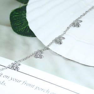 Peut inclure: Un bracelet de cheville argenté orné de petits charms en forme de cerises. La chaîne fine porte plusieurs pendentifs cerises espacés régulièrement. Les cerises présentent un design détaillé, ajoutant une touche fantaisiste au bijou.