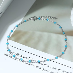 May include: A silver anklet with turquoise beads. The fine chain is adorned with small, round, turquoise beads. The anklet is displayed on a white surface with text that reads "Search for knowledge read more, sit on your..."
