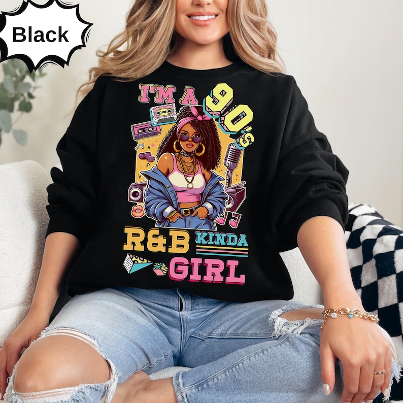 May include: Black sweatshirt with a colorful graphic featuring a woman with sunglasses, a pink top, and a blue jacket. The text reads "I'm a 90's R&B Kinda Girl" with retro music-themed illustrations.