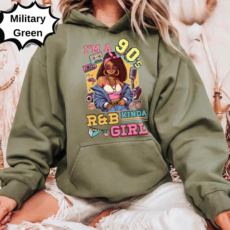 May include: Military green hoodie with a graphic that says "I'm a 90's Kinda R&B Girl." The graphic features a cartoon woman, a boombox, and a microphone. The hoodie has a front pocket and a drawstring hood.