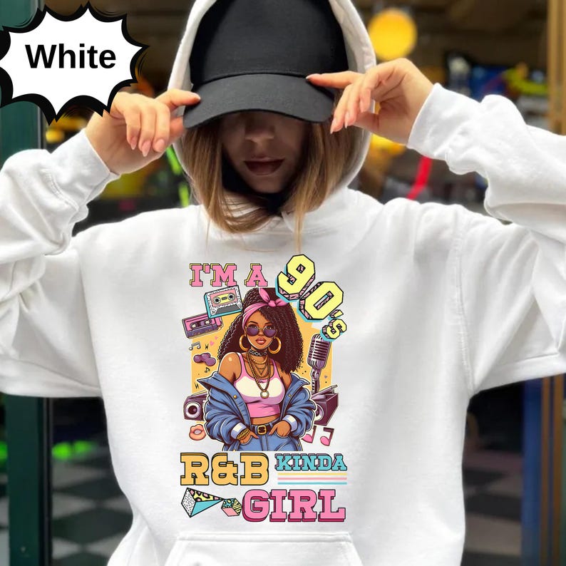 May include: White hoodie with a graphic featuring a cartoon woman with large hoop earrings, a pink top, and a blue jacket. The graphic includes the text "I'm a 90's R&B Kinda Girl" with cassette tapes and a microphone.