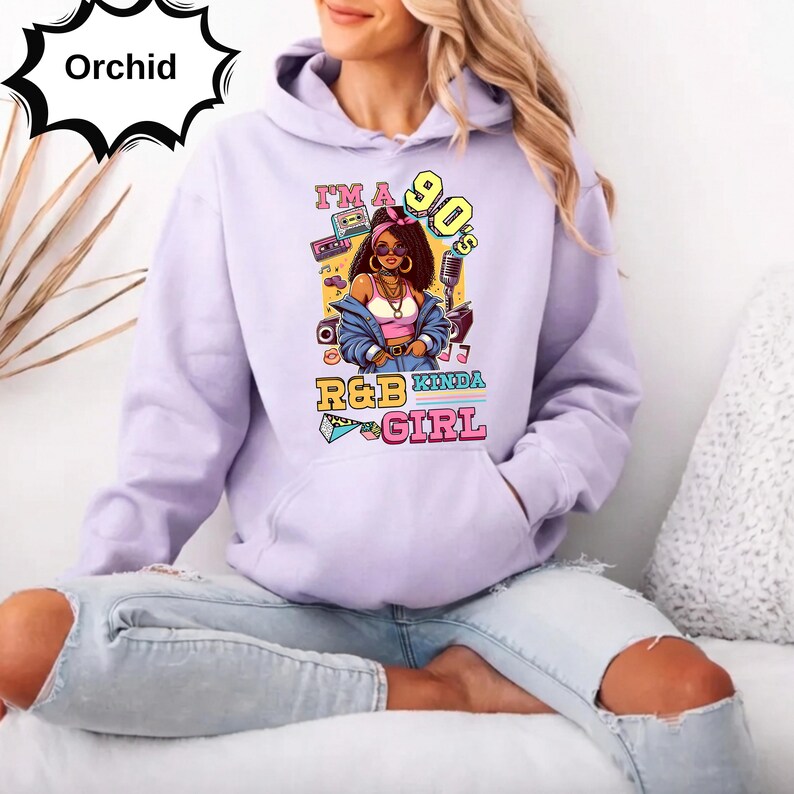 May include: A light purple hoodie with a graphic that says "I'm a 90's R&B Kinda Girl." The graphic features a cartoon woman with sunglasses, a boombox, and a microphone. The hoodie has a front pocket and a drawstring hood.
