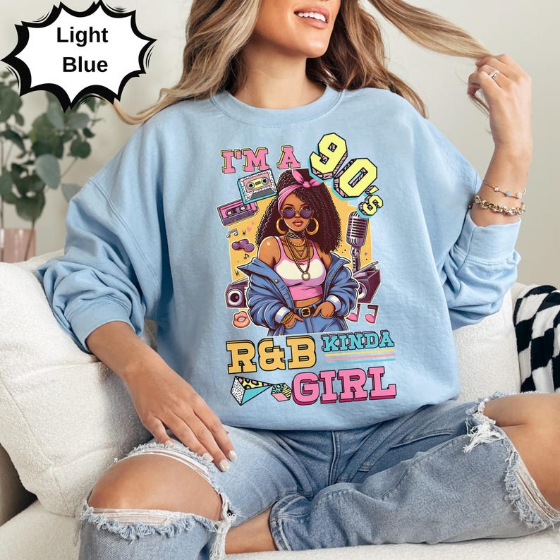 May include: Light blue sweatshirt with a graphic of a woman in 90s style, with the text "I'M A 90'S R&B KINDA GIRL". The graphic includes a boombox, microphone, and sunglasses.