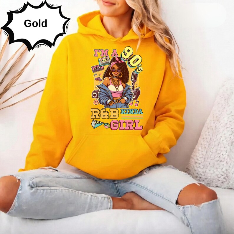 May include: A gold hoodie with a graphic that reads "I'm a 90's R&B Kinda Girl." The graphic features a cartoon woman with sunglasses, a boombox, and a microphone. The hoodie has a drawstring hood and a kangaroo pocket.