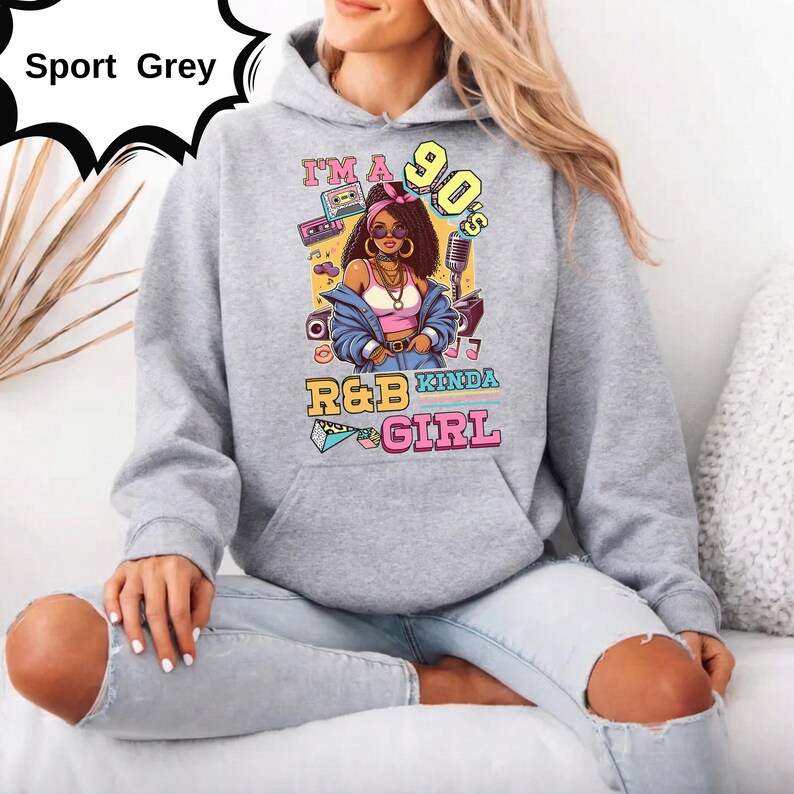 May include: Sport Grey hoodie with a graphic of a woman with the text "I'm a 90's R&B Kinda Girl". The design includes a boombox, microphone, and other 90s-themed elements. The hoodie is a light grey color.