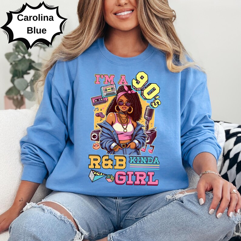 May include: Carolina blue sweatshirt with a graphic of a woman in sunglasses, a pink headband, and gold jewelry. The graphic includes the text "I'm a 90's R&B Kinda Girl" with a boombox and microphone.