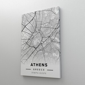 May include: A monochrome canvas print featuring a detailed map of Athens, Greece. The city's layout is shown in black lines. The name "ATHENS" and "GREECE" are printed below, along with the coordinates 37.967°N / 23.727°E.