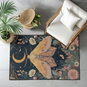 May include: A rectangular area rug featuring a large moth design with a crescent moon and floral elements. The rug has a dark blue background with a moth in shades of orange and pink. The rug is surrounded by flowers and greenery.