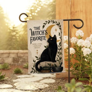 Könnte beinhalten: Eine rechteckige Gartenflagge mit einer schwarzen Katze, die auf einem Steinblock sitzt. Der Text lautet THE WITCH'S FAVORITE NINE LIVES. ENDLESS MAGIC. Das Design zeigt einen goldenen Halbmond, grüne Ranken, einen Mörser und Bücher.