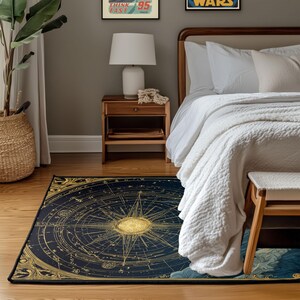 May include: A navy blue and gold compass rose rug with intricate celestial details. The rug features a central compass design with radiating lines and star patterns, framed by a decorative border. The rug is placed on a wooden floor in a bedroom setting.