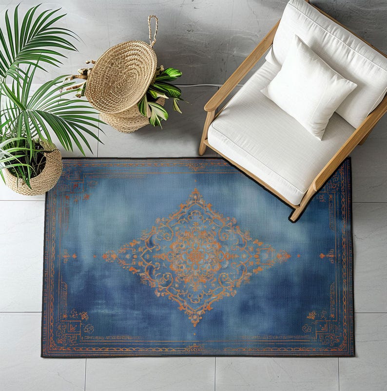 May include: Overhead view of a blue and orange patterned rug. The rug has a central diamond-shaped design and a border with intricate details. A white chair with a pillow is on the right. A potted plant and a woven basket are on the left.