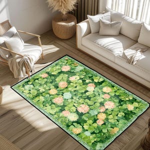 Op de afbeelding: Rechthoekig vloerkleed met een aquarelontwerp van groene klavers en kleurrijke bloemen. Het vloerkleed heeft een zwarte rand en ligt op een houten vloer. Het ontwerp van het vloerkleed bevat tinten groen, roze en geel.