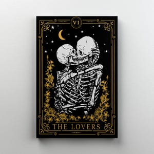 May include: A black and gold tarot card print featuring two skeletons embracing. The card is titled "THE LOVERS" and includes a crescent moon, stars, and floral accents. The card is framed with a gold border and the number "VI".