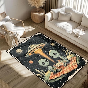May include: A rectangular area rug featuring a space-themed illustration. The design includes a UFO emitting a beam of light, planets, stars, and two green aliens enjoying a picnic on a checkered blanket. The rug has a black border.
