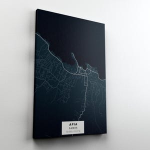 May include: A canvas print of Apia, Samoa, featuring a detailed white map against a dark blue background. The city's name and coordinates are displayed in a white rectangle at the bottom. The artwork is mounted on a white wall.