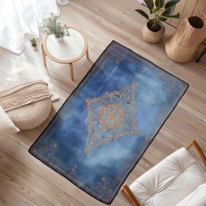 May include: A rectangular blue rug with an ornate orange and gold central design. The rug has a dark border and a faded, watercolor-like appearance. The rug is placed on a hardwood floor.