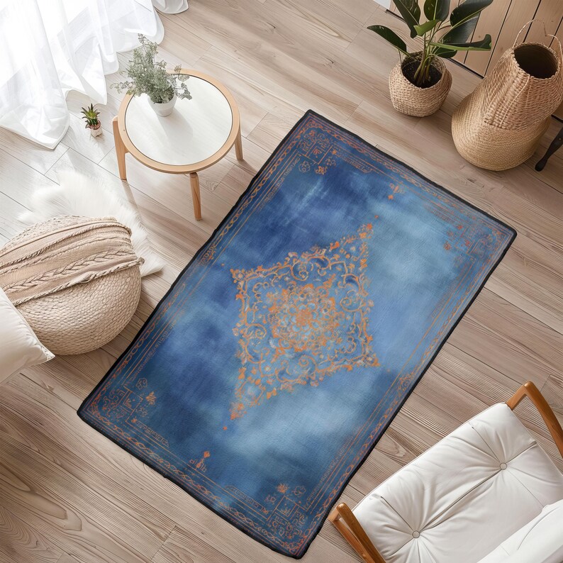 May include: A rectangular blue rug with an ornate orange and gold central design. The rug has a dark border and a faded, watercolor-like appearance. The rug is placed on a hardwood floor.