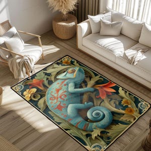 Op de afbeelding: Een rechthoekig vloerkleed met een gedetailleerde illustratie van een blauwe kameleon met rode markeringen, omringd door bloemen- en bladmotieven in groen, oranje en geel. Het vloerkleed heeft een donkere rand en ligt op een houten vloer.