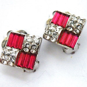 May include: A pair of silver tone clip-on earrings with a geometric design. The earrings feature red and clear rhinestones.