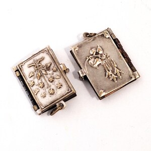 May include: Two small, open silver lockets with floral designs. The lockets are rectangular with hinged sides and a clasp. One features a bouquet, the other a heart and bell-shaped flowers. The hinges and clasps are gold-toned.