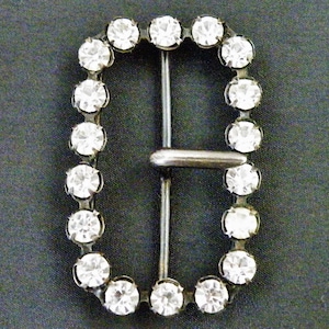 Peut inclure: Une boucle argentée avec un cadre rectangulaire orné de strass transparents.