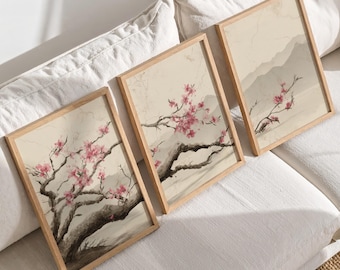 May include: Three framed art prints featuring watercolor illustrations of cherry blossom branches with pink flowers and dark brown branches. The artwork has a beige background and is set in light brown wooden frames.